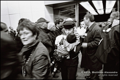 Dramatic picture of a French airline stewardess holding a child refugee in a busy airport. Picture is a link to www.FreePhotoCourse.com's Photographer Profiles series.  Photo Credit: Matthieu Alexandre, (c) 2010, all rights reserved.  
