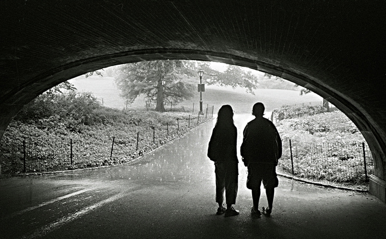 Picture of a young couple, silhouetted, taking shelter from the rain under a Central Park bridge.  Photo Credit: Joe Constantino.  Part of the popular online photography exhibit, NYC Exposed, from http://www.FreePhotoCourse.com.  All rights reserved.