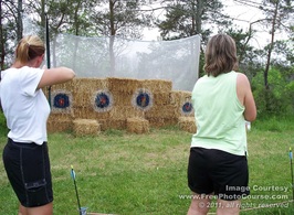Picture of two women practicing archery.  Bow & Arrow with targets on bales of hay; © 2011, FreePhotoCourse.com, all rights reserved 