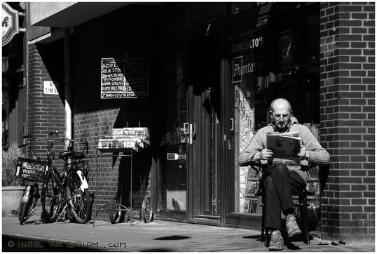 Contributor's Photo Gallery - Spring Photo Challenge - picture of a shop owner reading a book outside his establishment in Amsterdam.  Free Photo Lessons at www.FreePhotoCourse.com.© 2011, all rights reserved.  
